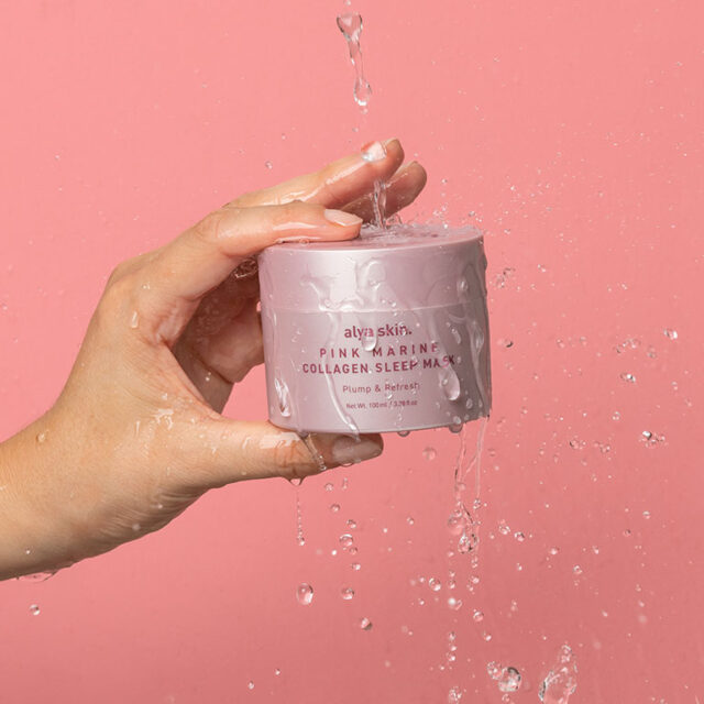 Alya Skin Pink Marine Collagen Sleep Mask jar in hand with water drops and pink background